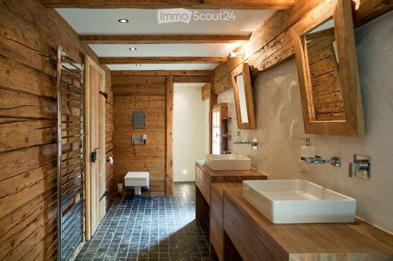Bathroom with wooden walls, two sinks, a toilet, and a mirror. Features a towel rack and wooden cabinetry.