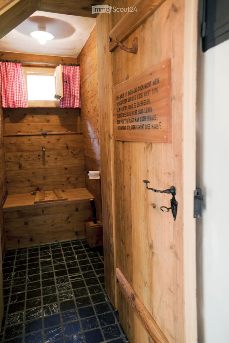 Wooden bathroom with a bench, toilet paper, and a window with red checkered curtains.
