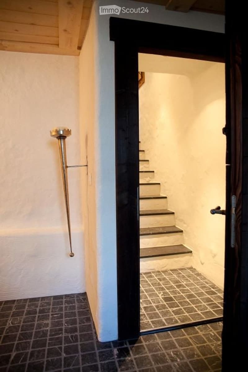 A narrow hallway with a staircase leading upwards, featuring a modern wall-mounted light fixture and a glass door at the end.