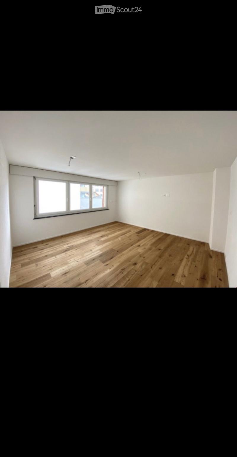 Empty room with wooden flooring, white walls, and a large window letting in natural light.