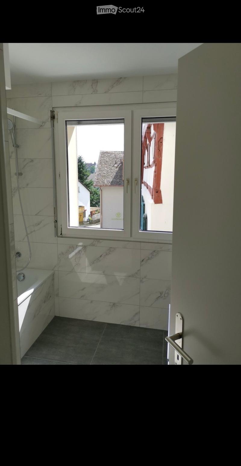 Modern bathroom with marble tiles, bathtub, shower, and large windows offering a view of the street.