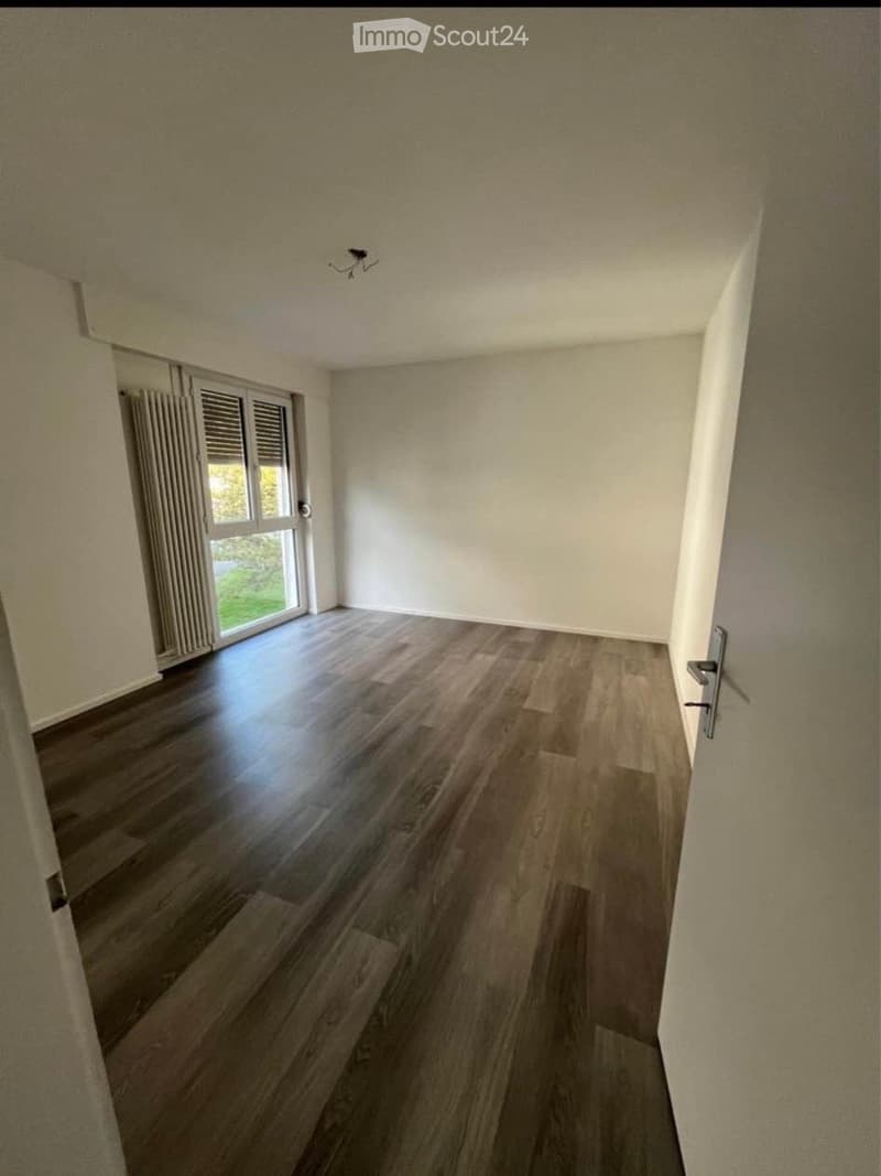 Empty room with wooden flooring, white walls, and a large window with blinds. No furniture or equipment is present.