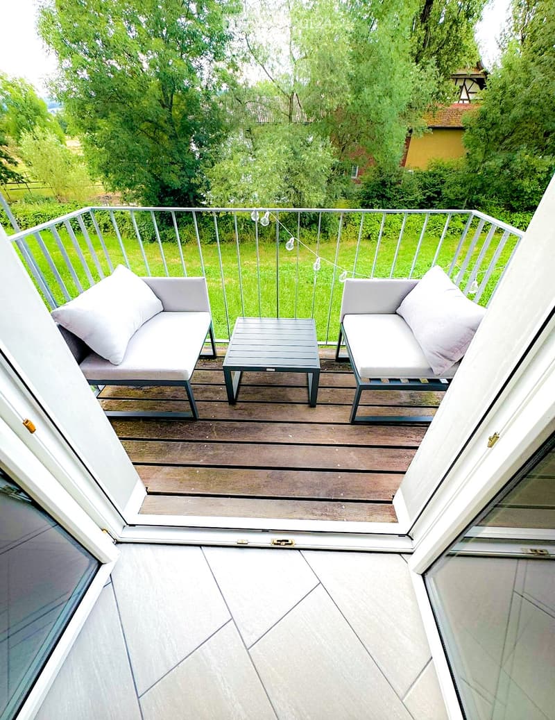 Balcony with wooden decking, metal railing, two grey sofas, and a small table.