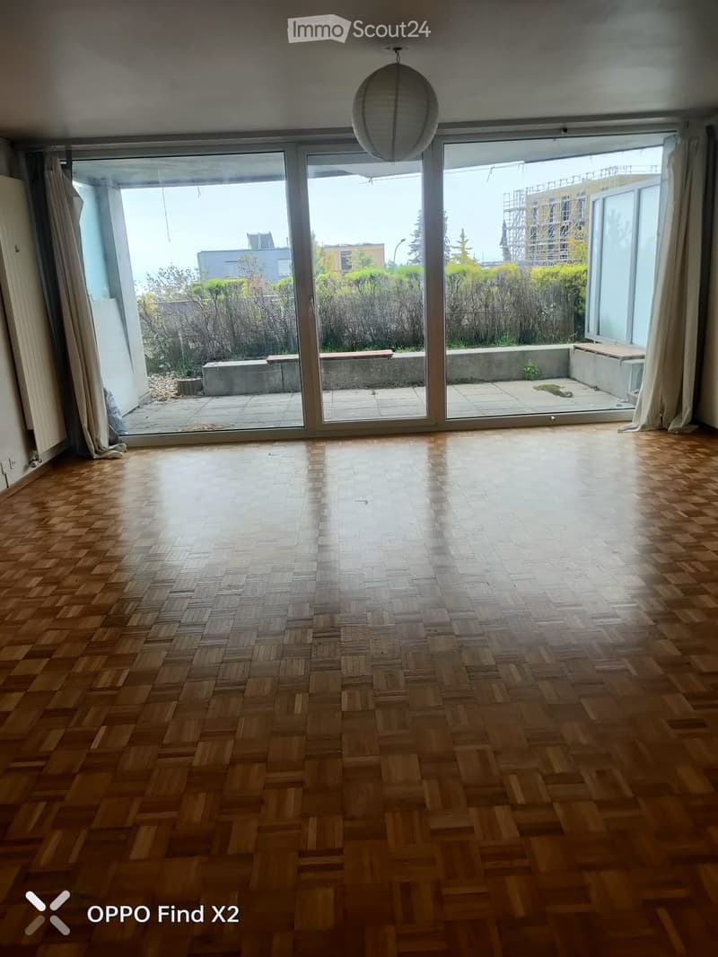 Empty room with wooden herringbone flooring, large sliding glass doors leading to a patio area, and a hanging paper lantern light fixture.