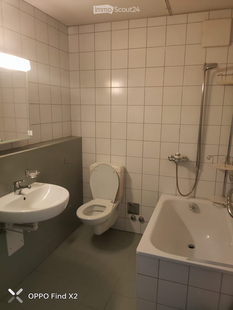 Bathroom with white tiles, a sink, toilet, bathtub, and a mirror above the sink.