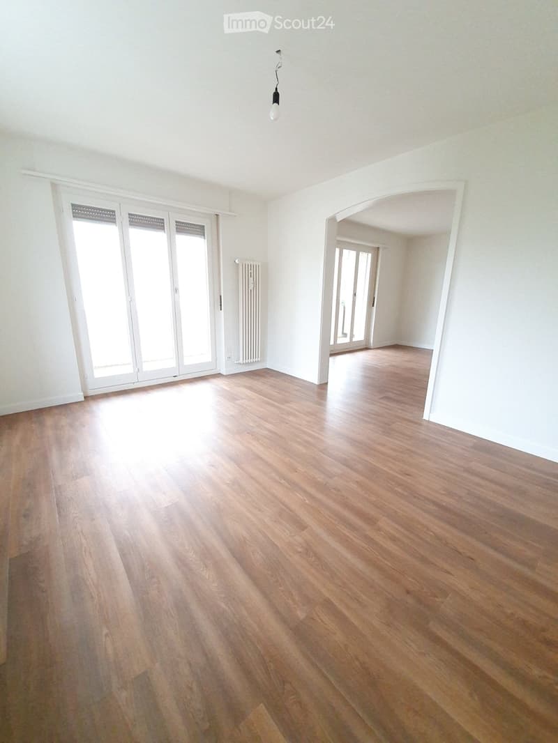 Empty room with wooden flooring, white walls, large sliding glass doors, and a visible radiator. No furniture or equipment present.