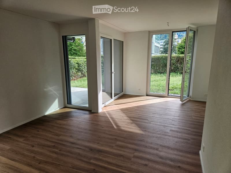 Empty room with wooden flooring and large sliding glass doors leading to a garden area.