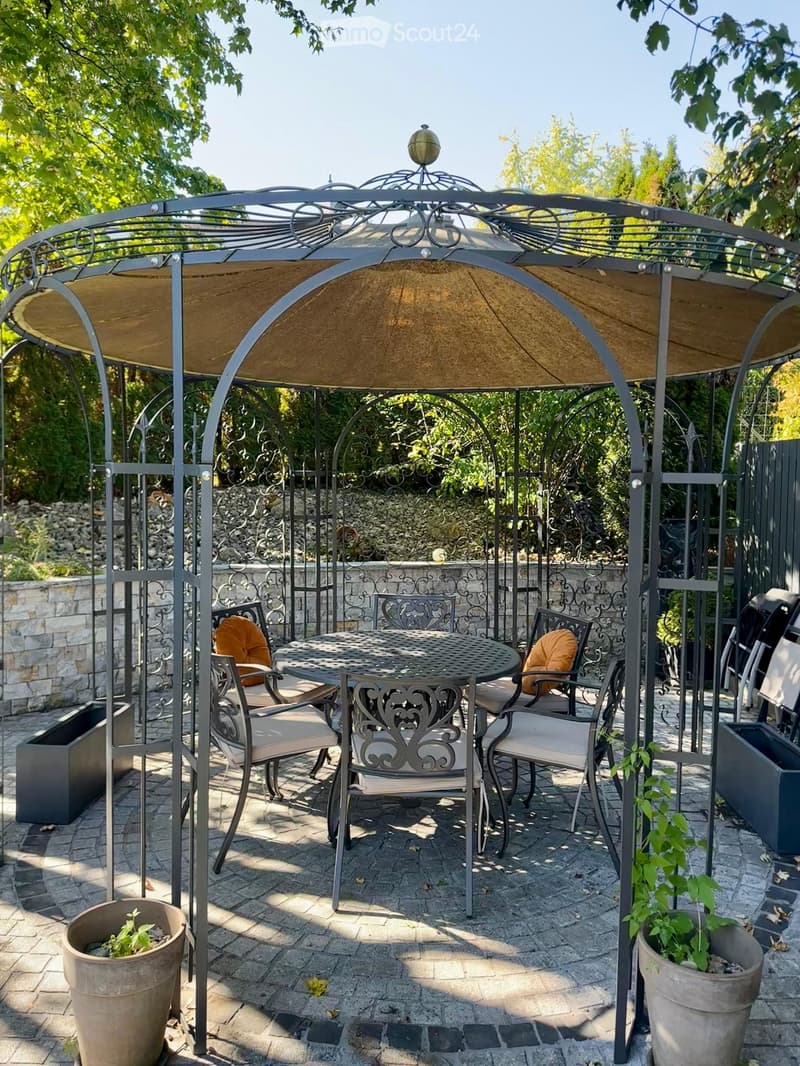 Outdoor patio with a metal gazebo, round table, four chairs, and potted plants.