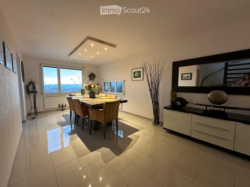 Modern dining room with a large dining table, chairs, sideboard, and decorative vases. Large windows offer a scenic view.
