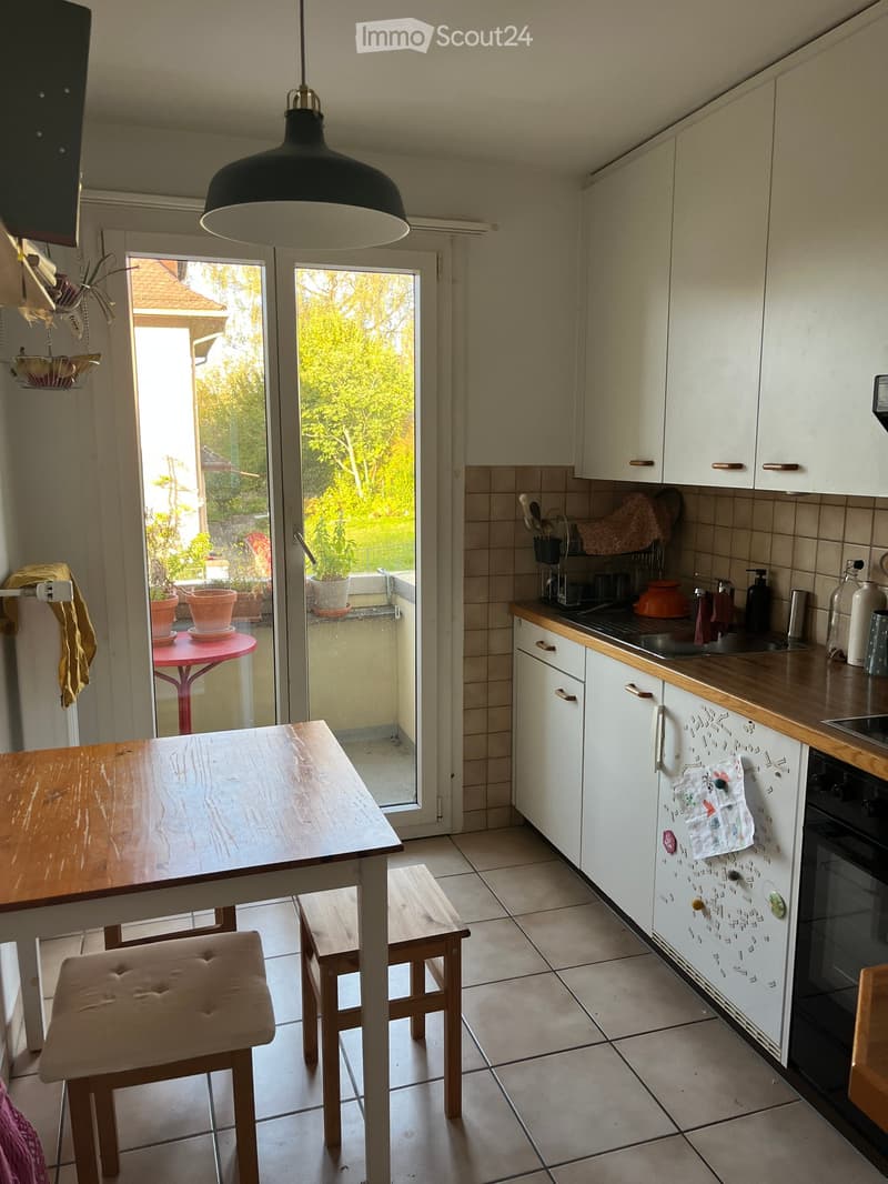 Bright kitchen with white cabinets, wooden countertop, and a dining table with stools. A large sliding glass door offers a view of a garden.