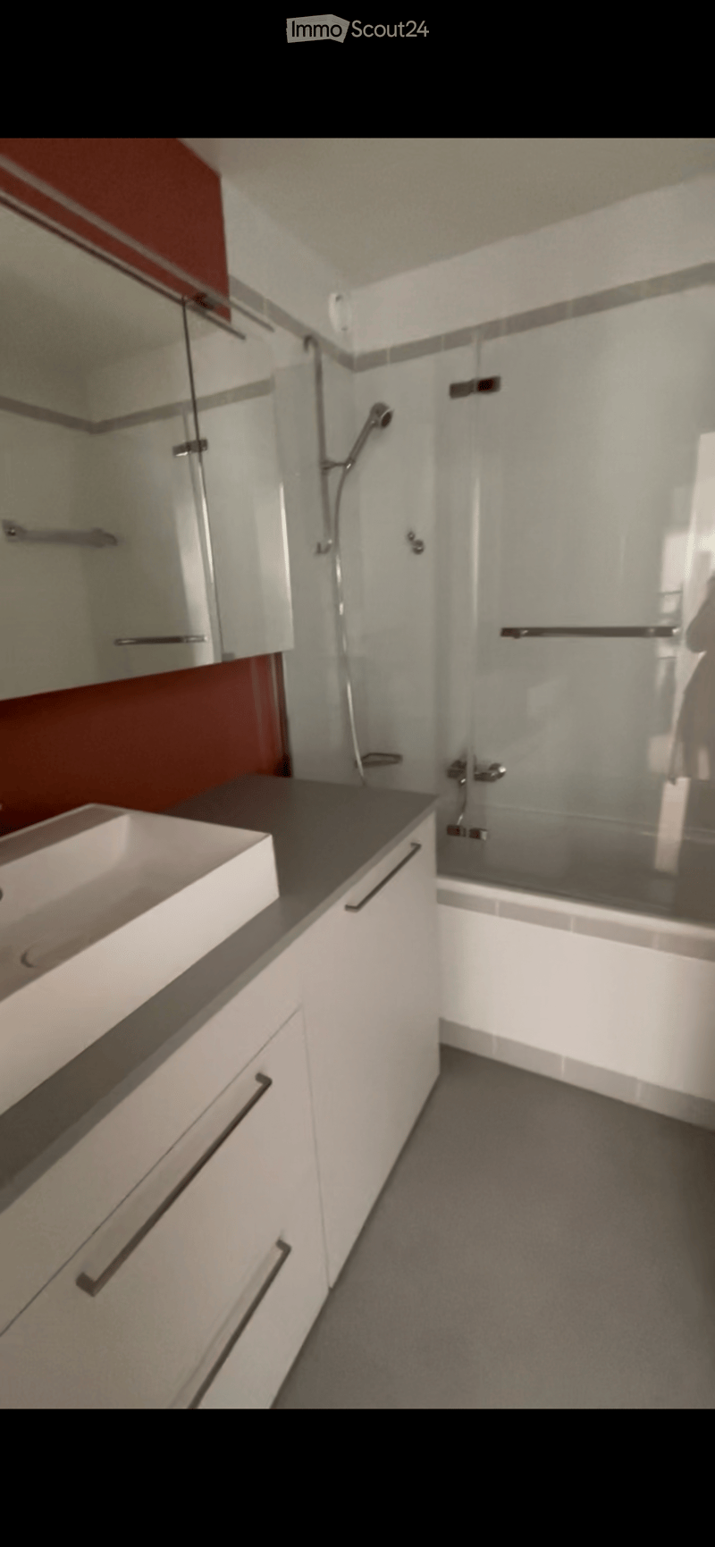 Modern bathroom with white cabinets, a dark countertop, a white sink, and a glass-enclosed shower area with a modern faucet.
