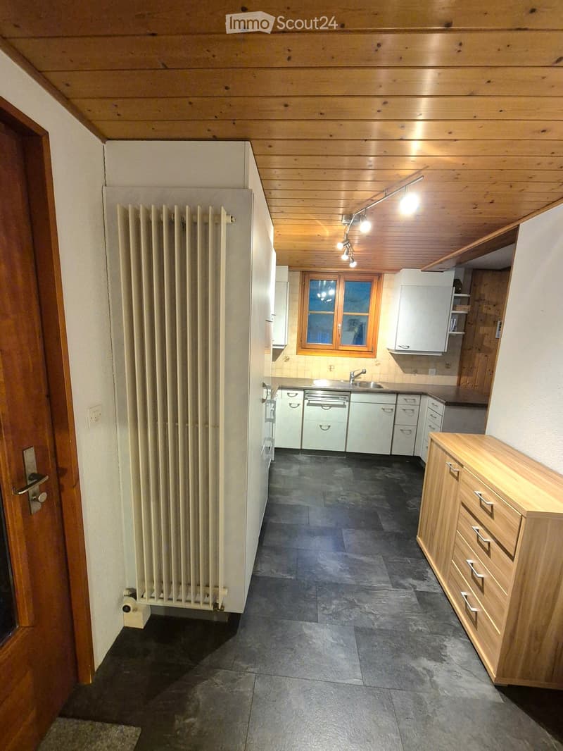 Kitchen with wooden ceiling, dark tiled floor, white cabinets, sink, and radiator.