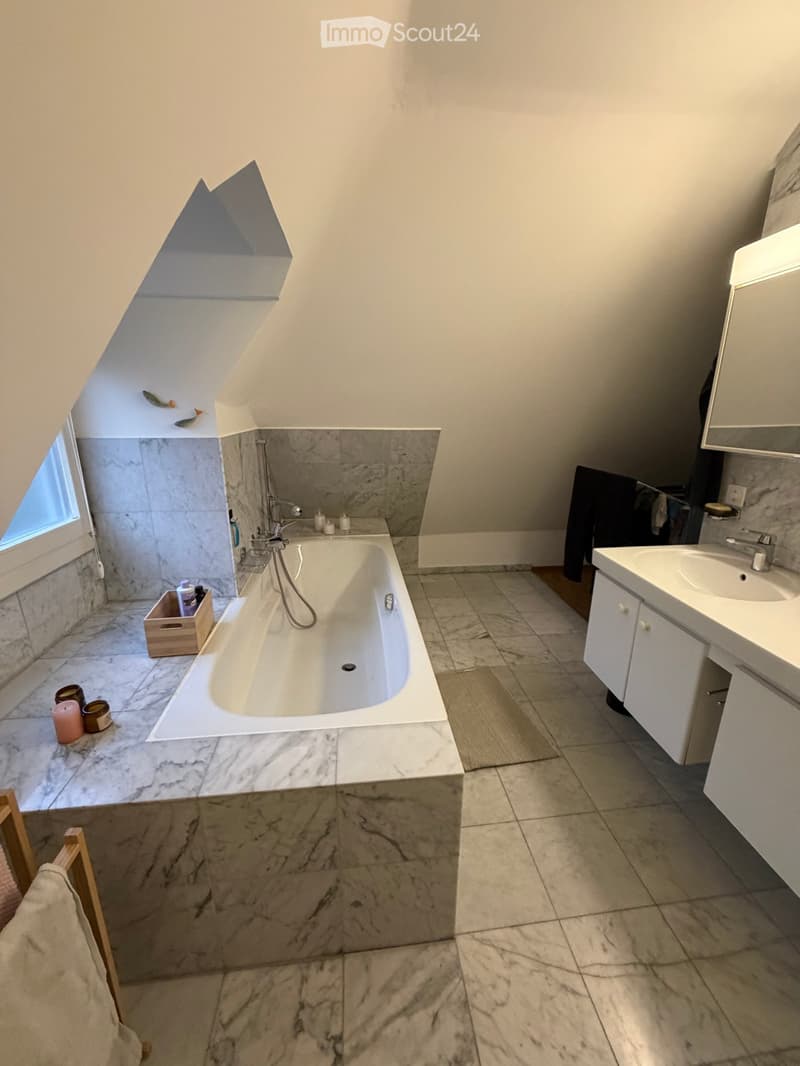 Modern bathroom with a freestanding bathtub, marble tiles, a sink with a mirror, and a small wooden crate holding toiletries.
