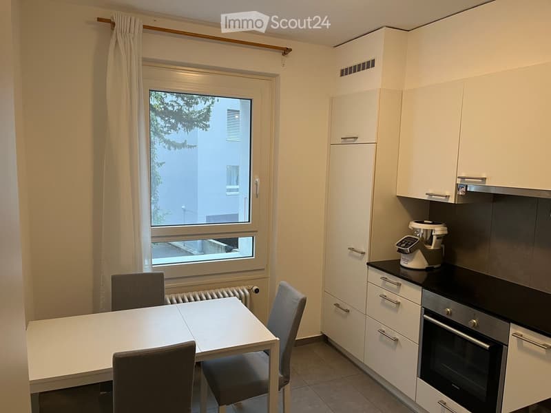 Modern kitchen with white cabinets, a dining table with chairs, and a window overlooking a building.