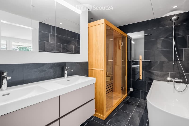 Modern bathroom with black tiled walls, a white sink with a modern faucet, a bathtub, a glass-enclosed wooden shower, and a large mirror above the sink.