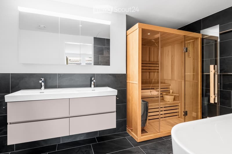 Modern bathroom with a double sink, large mirror, and a wooden sauna unit.