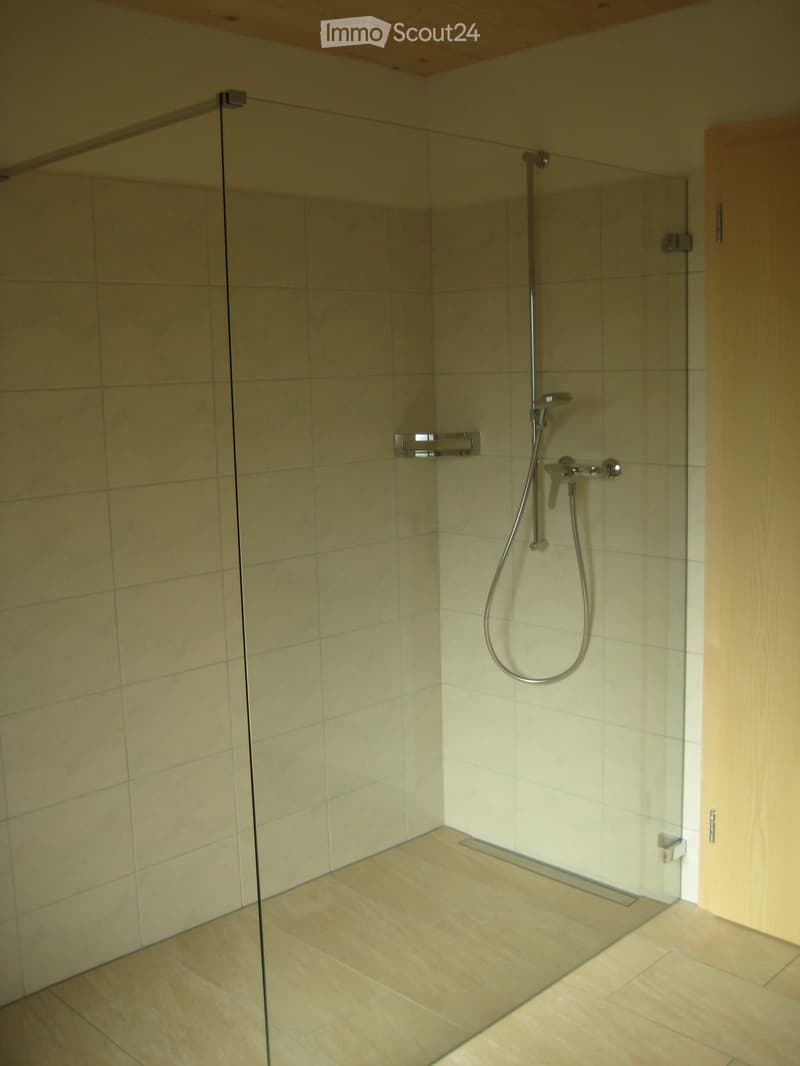 Modern shower area with glass enclosure, beige tiles, and a handheld shower hose.