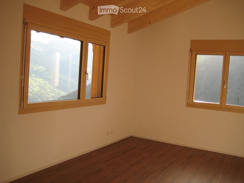 Empty room with wooden flooring, light-colored walls, and large windows offering a scenic mountain view.