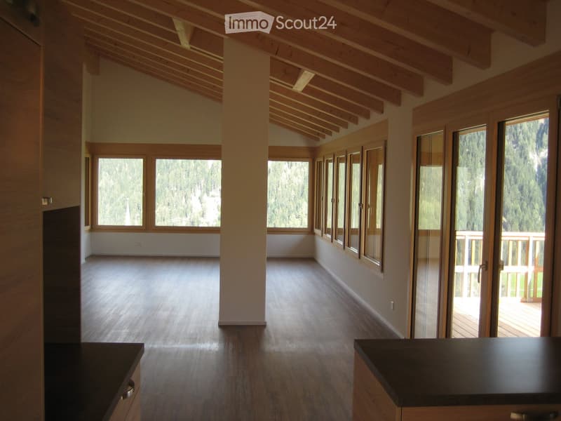 Open, unfurnished room with wooden floors, exposed wooden beams, large windows, and a balcony area with a wooden deck.