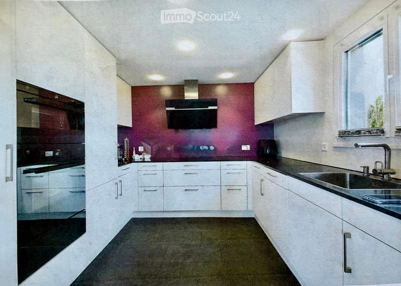 Modern kitchen with white cabinets, stainless steel sink, and appliances, featuring a dark countertop and a colorful backsplash.