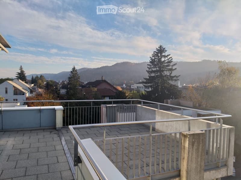 Roof terrace with tiled flooring, metal railings, and a scenic view of trees and distant hills.