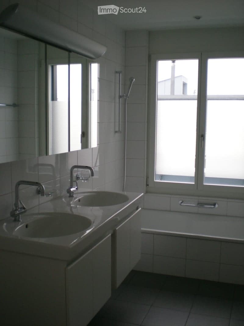 Modern bathroom with two sinks, a bathtub, and a showerhead, featuring large windows and tiled walls.