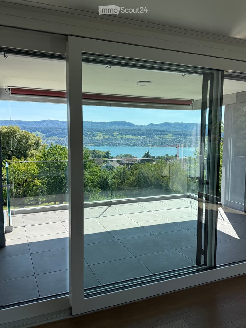 Modern balcony with large glass doors, tiled floor, and scenic view of a lake and mountains.