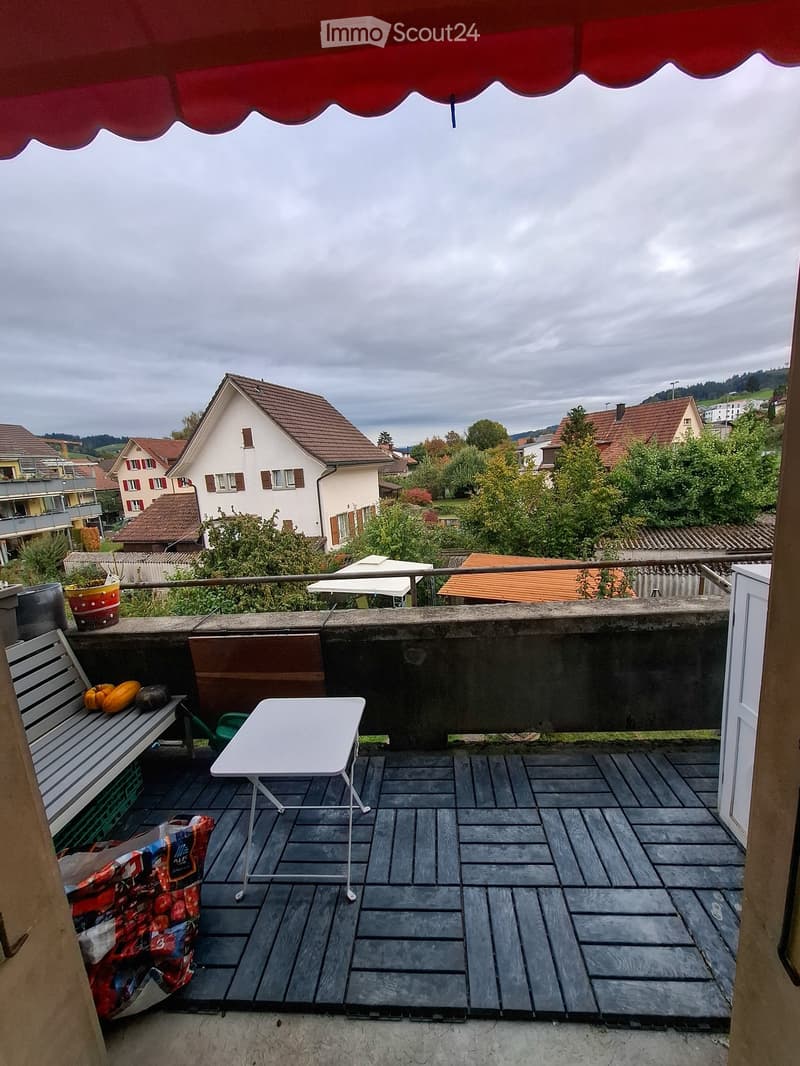 Balcony with wooden decking, white table, bench, and various items including a shopping bag and potted plants.