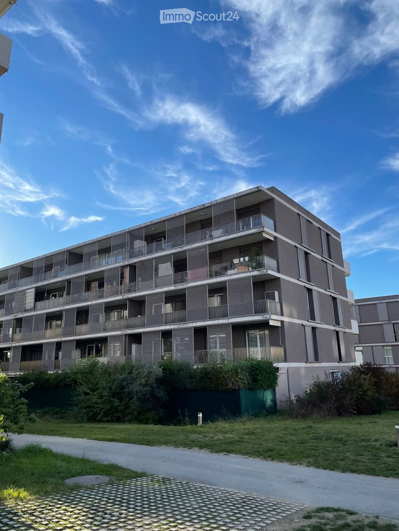 Multi-story residential building with balconies, modern facade, and surrounding greenery.