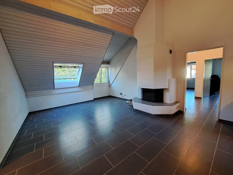 Empty room with dark tiled floor, white walls, and a built-in fireplace. The room features a slanted wooden ceiling and a skylight window.