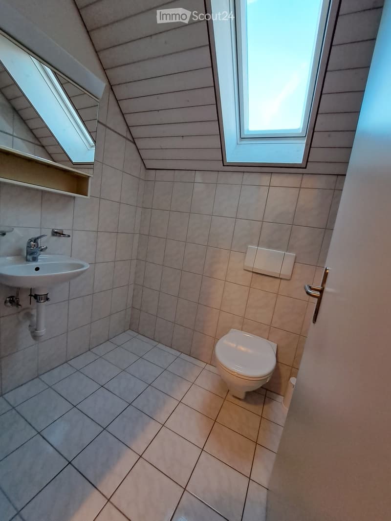 Small bathroom with tiled walls and floor, featuring a toilet, sink, and window with blinds.
