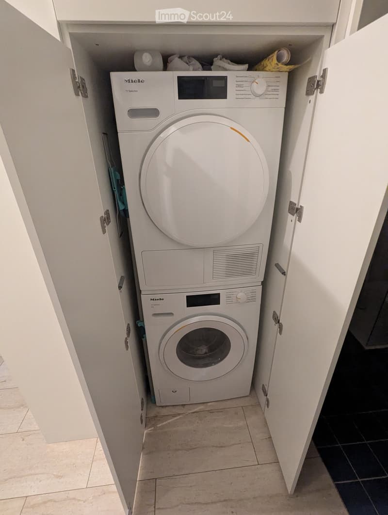 A compact laundry area with a stacked washing machine and dryer unit, white cabinetry, and tiled flooring.