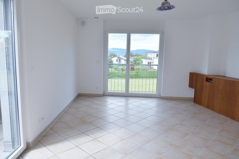 Empty room with tiled floor, white walls, large sliding glass doors leading to a balcony, and a wooden cabinet.
