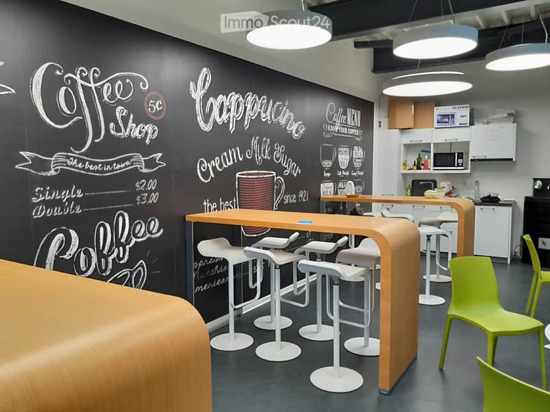 Modern coffee shop interior with a chalkboard menu wall, bar counter, white stools, and green chairs.