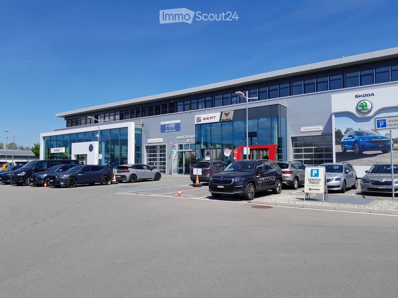 Modern car dealership building with large glass windows and signage for Volkswagen, Seat, and Skoda. Several cars are parked in front, and there is a parking sign visible.