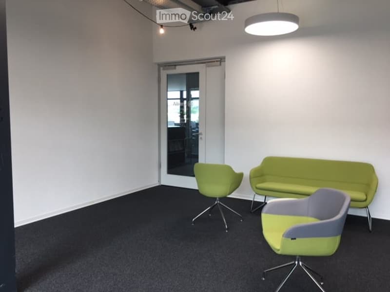 Modern, minimalist room with white walls, black carpet, and a large glass door leading outside. Features a green sofa and two matching green chairs.