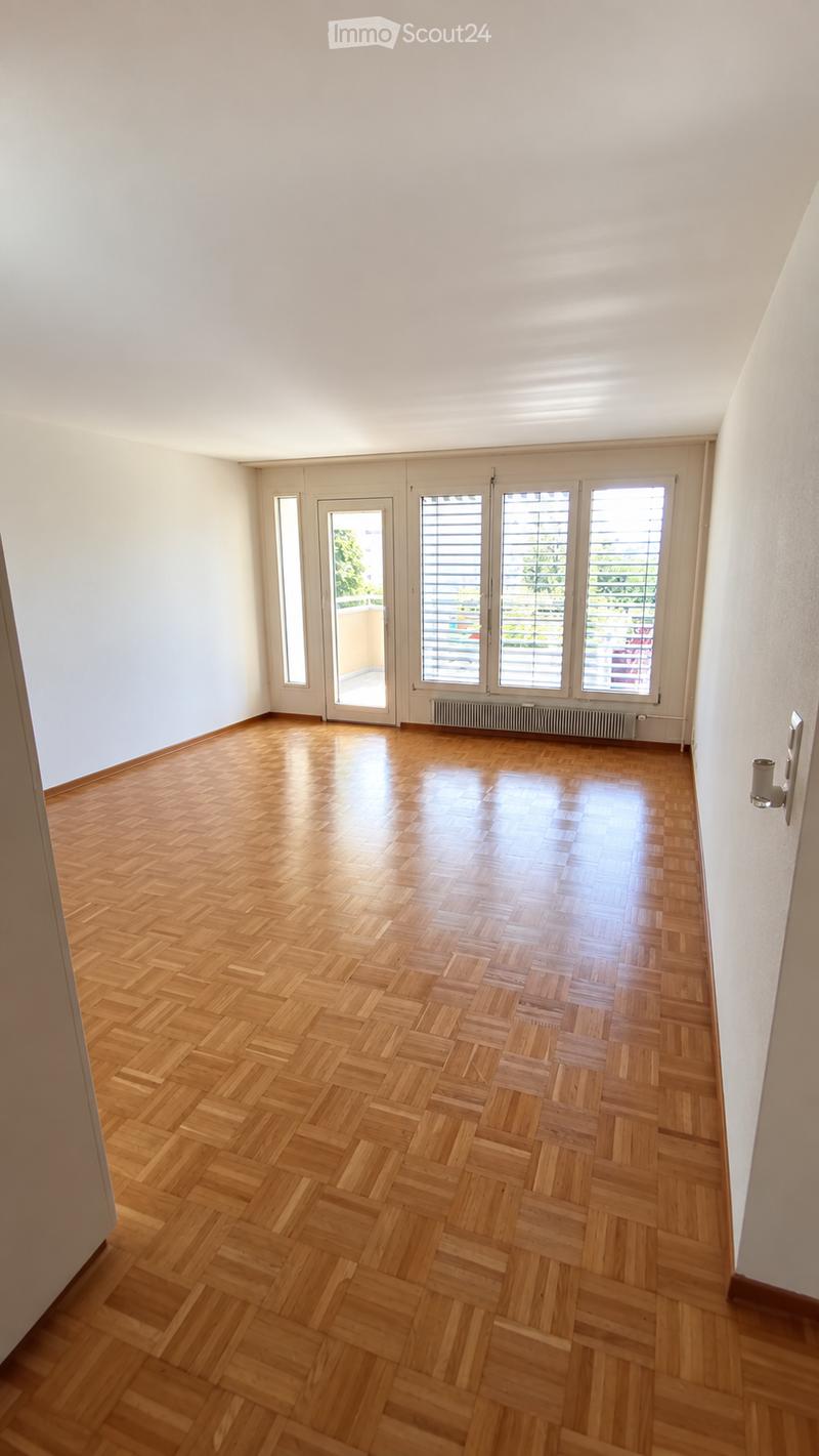 Empty room with wooden parquet flooring, white walls, large windows with blinds, and a radiator under the windows.
