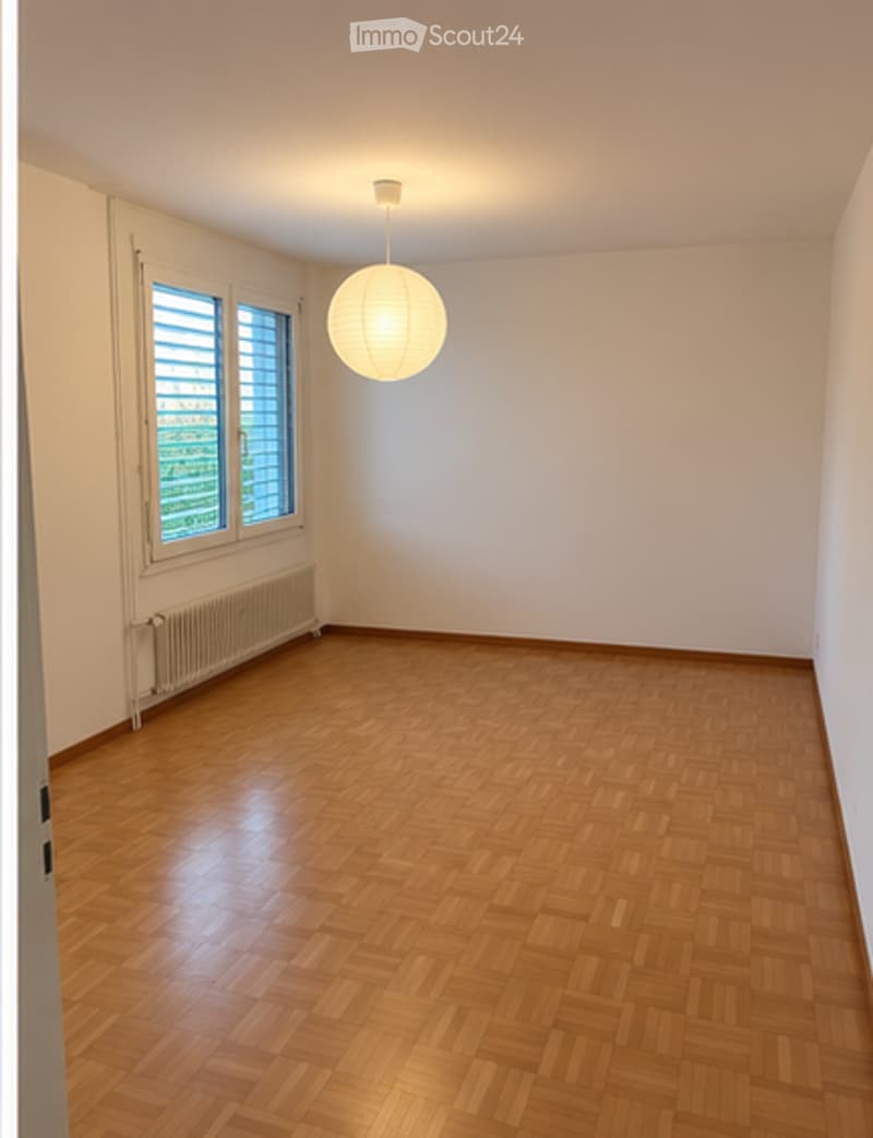 Empty room with wooden flooring, white walls, large window with blinds, and a hanging light fixture.