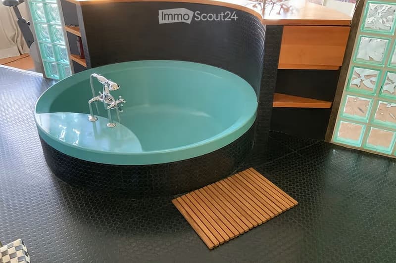Modern bathroom with a large, curved green bathtub, chrome faucet, and a wooden mat placed on the floor.