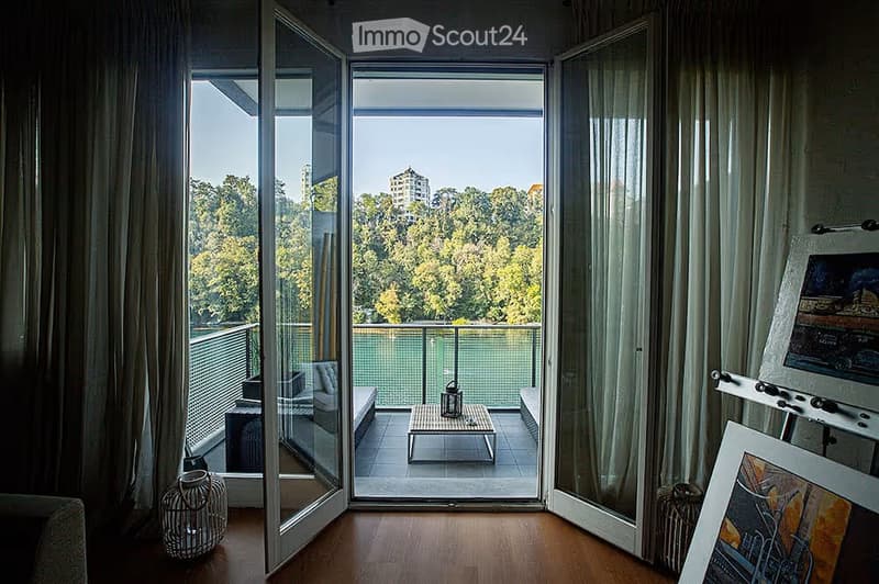 Modern living room with large glass doors opening to a balcony, featuring a sofa, small table, and decorative items.