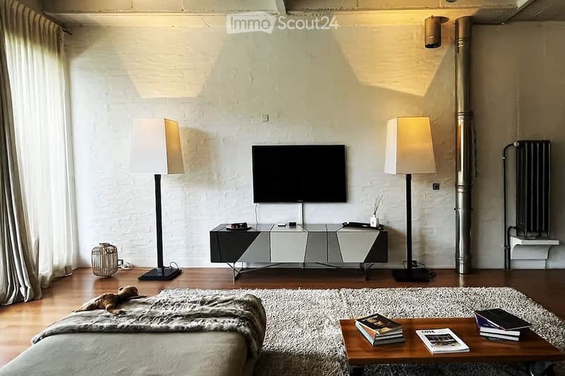 Modern living room with wooden flooring, white brick walls, large windows with curtains, a sofa with a fur throw, a coffee table with books, two floor lamps, a TV on a sleek stand, and a decorative basket on the floor.