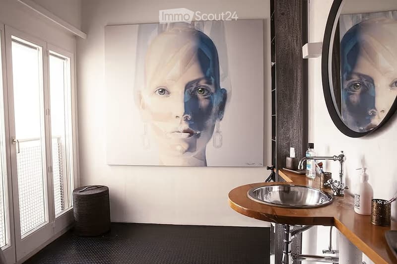 Modern bathroom with a large round mirror, wooden sink, and a large abstract portrait on the wall.