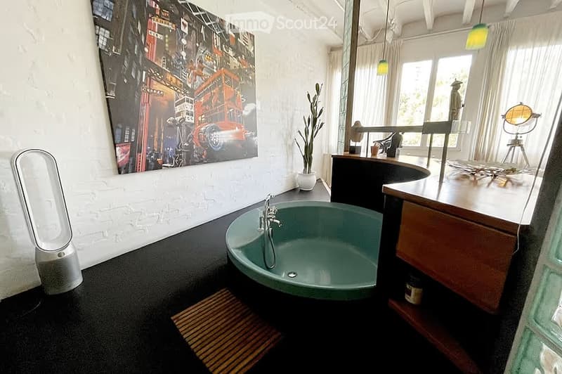 Modern bathroom with a freestanding bathtub, sleek faucet, large mirror, potted plant, and decorative artwork on the wall.