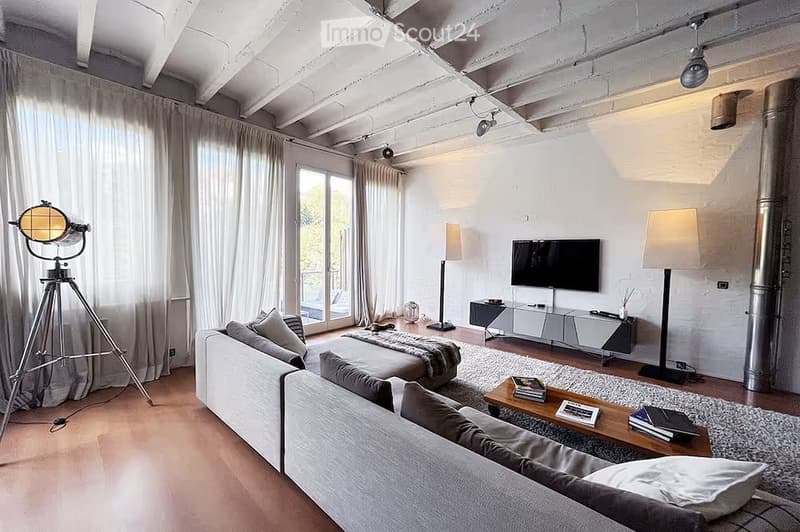 Modern living room with exposed wooden beams, large windows, grey sofa, coffee table, floor lamp, TV, tripod lamp, and ottoman.