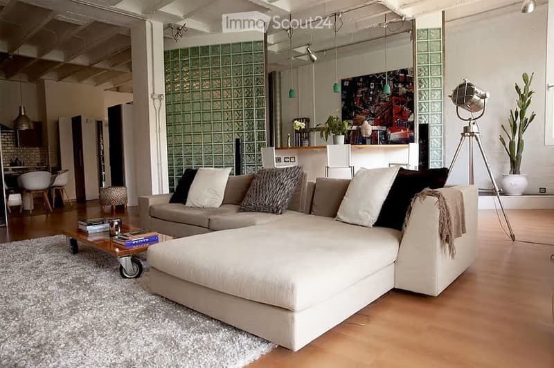 Modern living room with a large sectional sofa, coffee table with books, pendant lights, and a view into a kitchen area with bar stools.