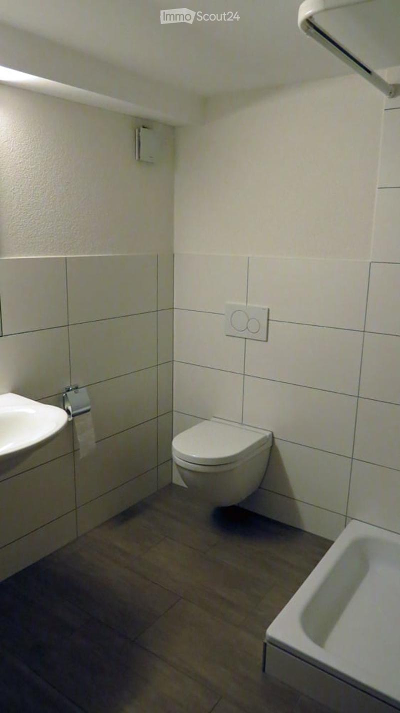 Bathroom with a white sink, a white toilet, a mirror, white tiles on the walls and wooden floor