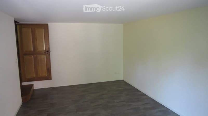 Empty room with a wooden door, white walls, and a gray floor