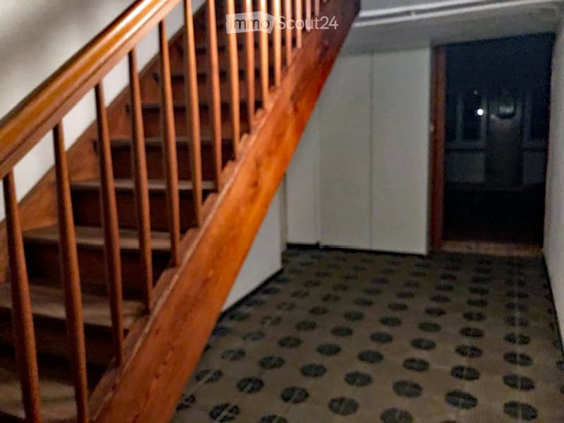 A dark and narrow hallway with wooden stairs leading to the upper floor.