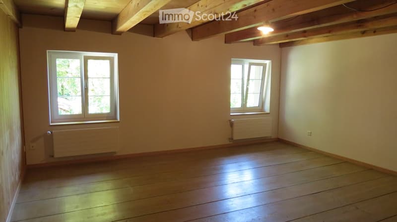 Empty room, hardwood floors, wooden beams, two windows, two radiators
