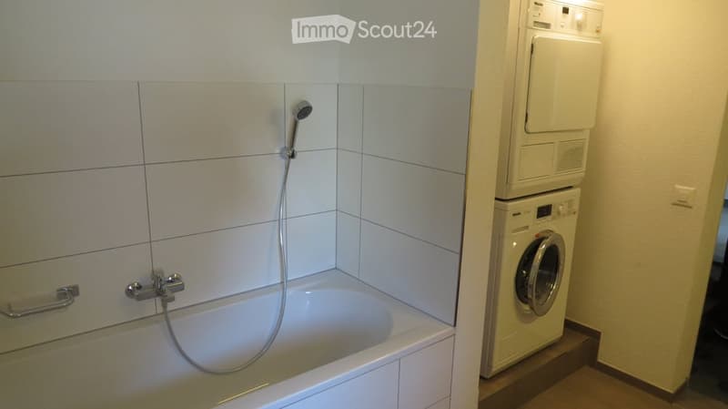 White bathtub, showerhead, stacked washing machine and dryer, white cabinets